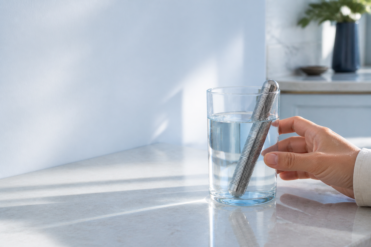 A hand reaching for a glass containing the Covarook rod in a sunlit kitchen